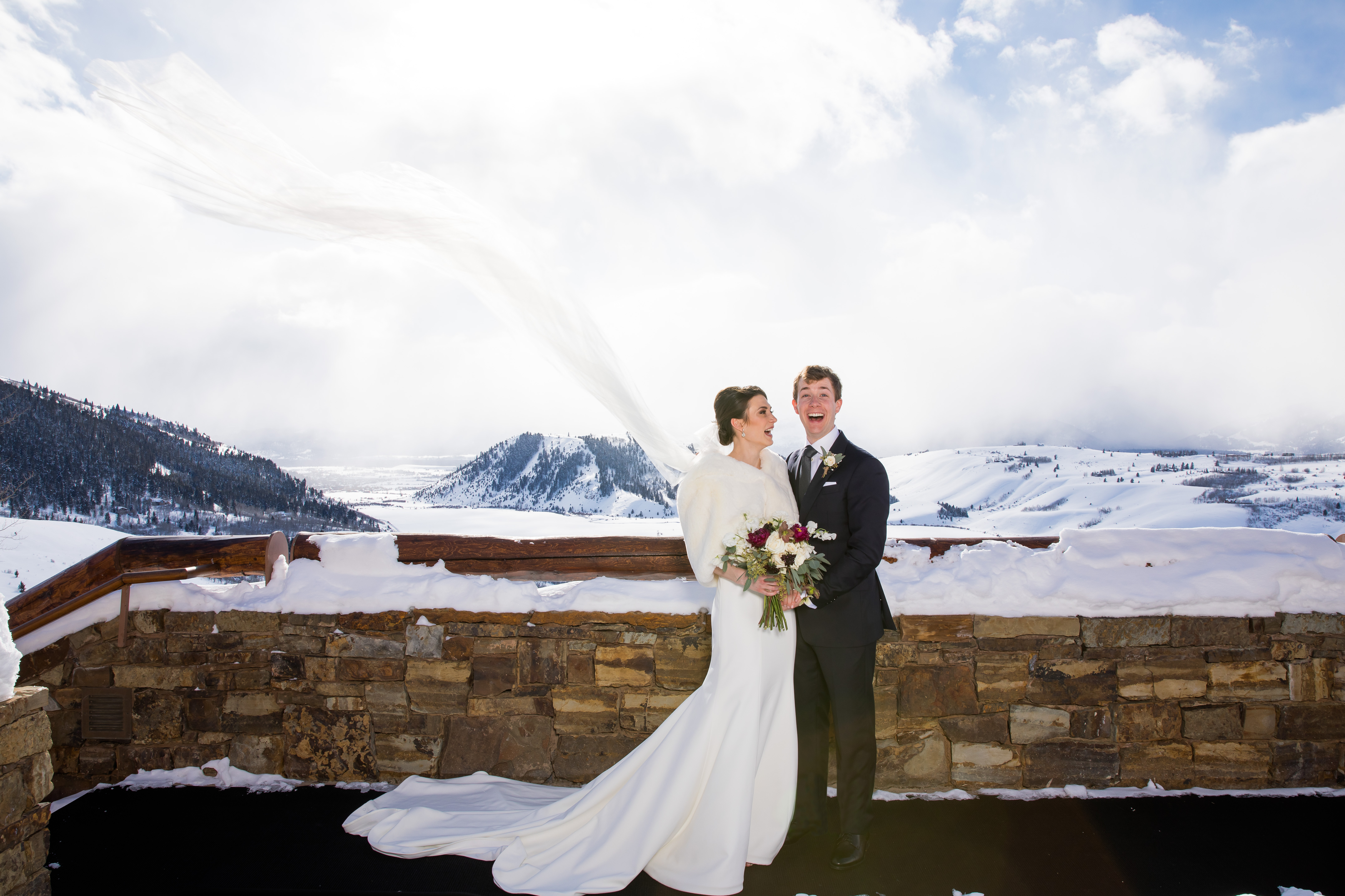 A bride and groom laugh as the winter wind sweeps her veil at the Amangani in Jackson Hole WY