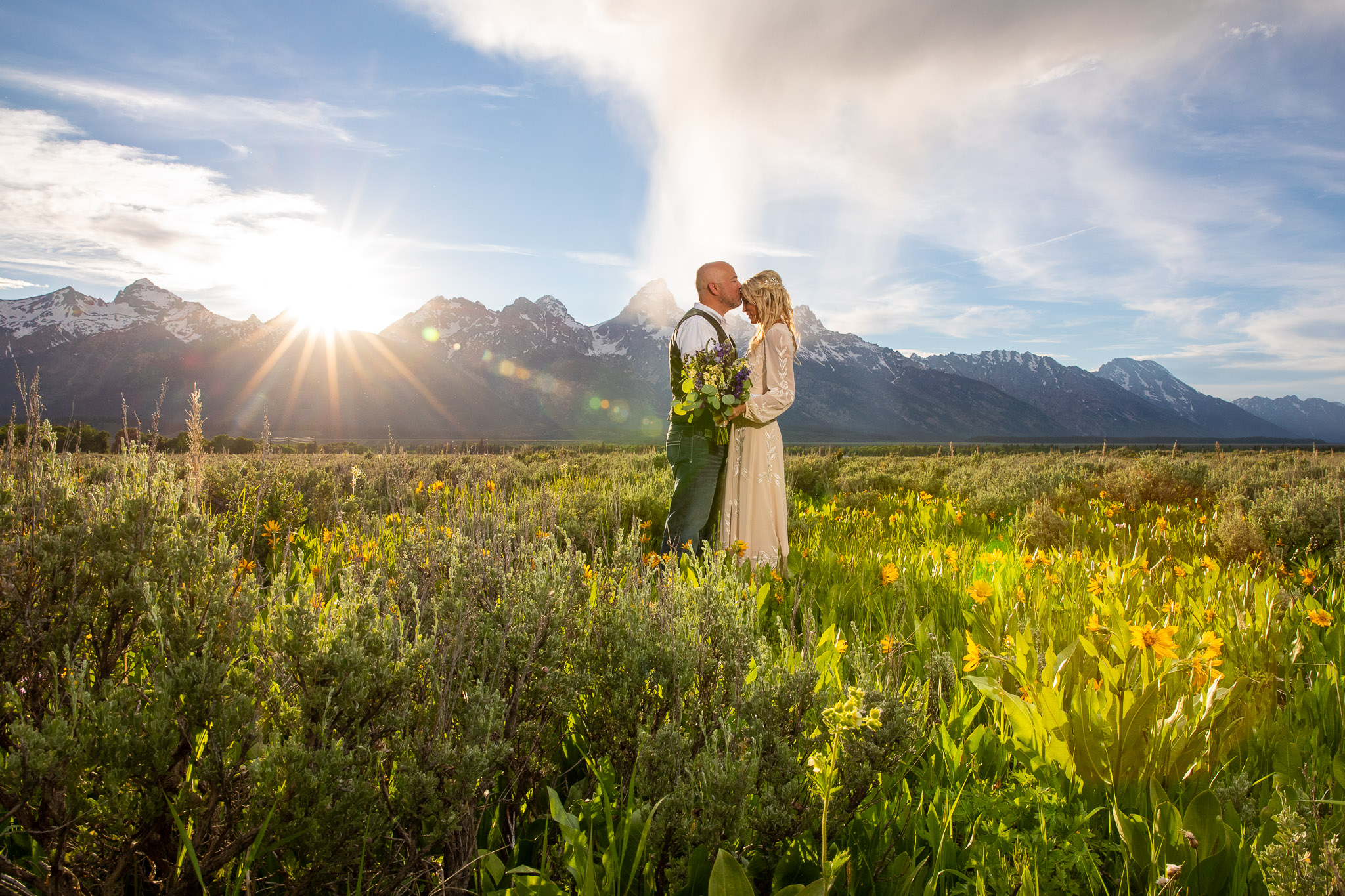 A Groom and Bride embrace at sunset in a field of flowers in Grand Teton National Park Wyoming