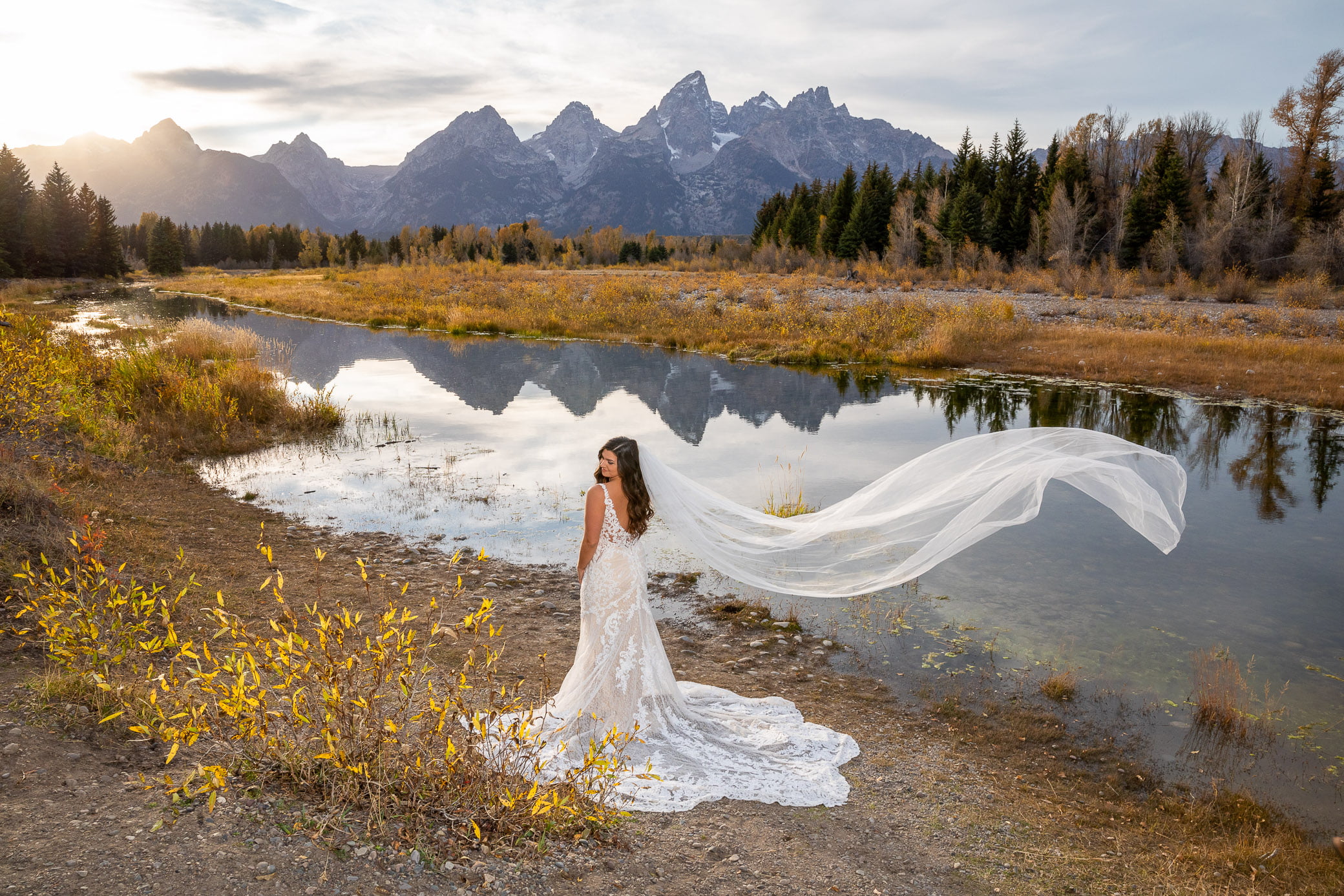 A bride wearing a wedding dress and a long veil basks in the beauty of Grand Teton National Park after her Jackson Hole wedding elopement